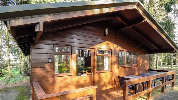 A wooden cabin with a deck, large windows, and a table and chairs.