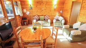 A cozy cabin interior with a wooden dining table, chairs, a sofa, and a television.