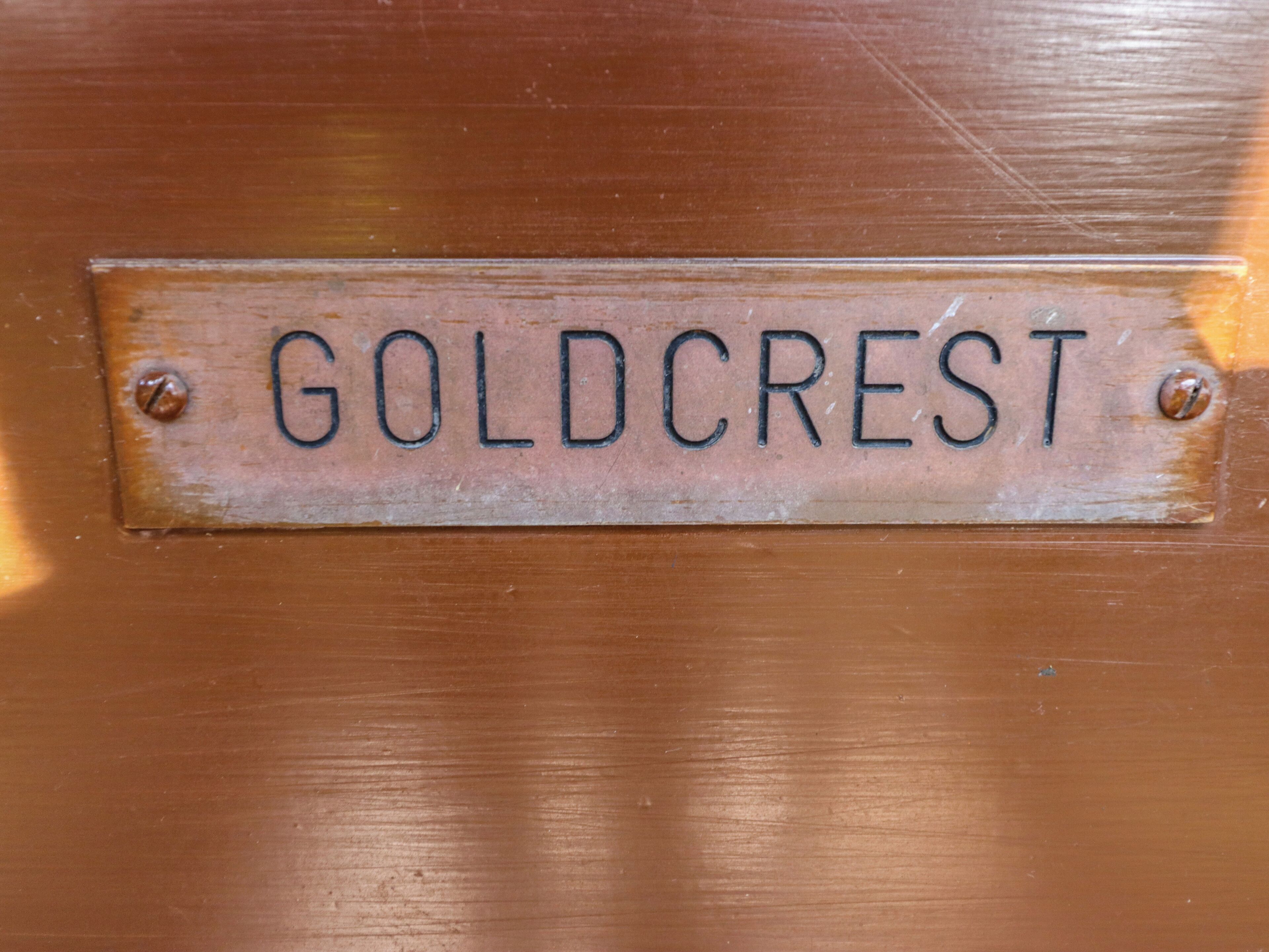 A metal plaque with the inscription "GOLDCrest" on a wooden surface.