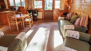 A cozy cabin interior with a wooden dining table, chairs, a sofa, and a television.