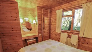 A wooden cabin room with a bed, a vanity with a mirror, and a window with curtains.