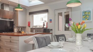 A modern kitchen with a skylight, a dining area with a table set for two, and a fruit market poster on the wall. - 15 Summerland Avenue (Dawlish)
