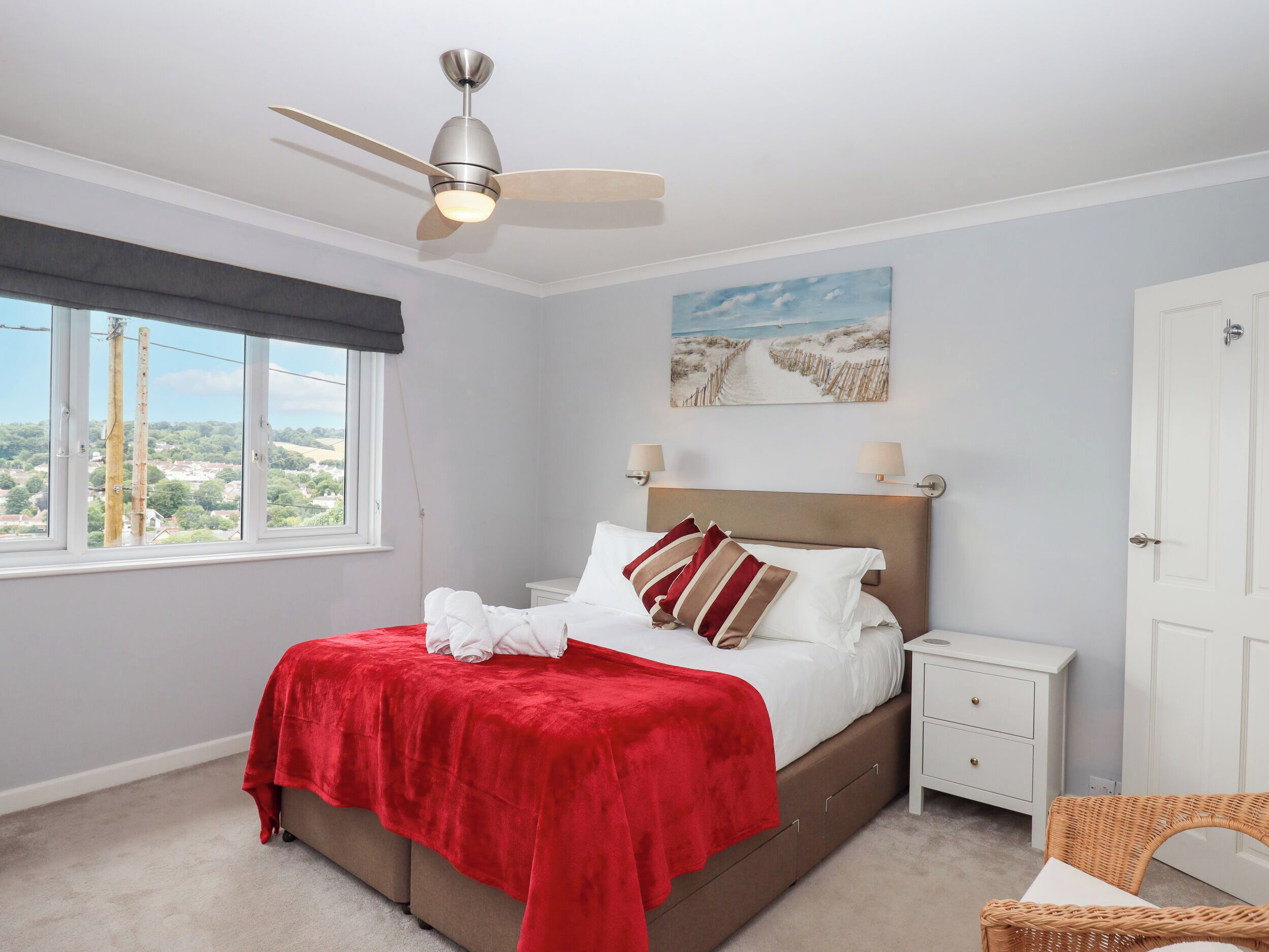 Une chambre à coucher comprenant un lit, une table de chevet, une chaise, un ventilateur de plafond, une fenêtre et un tableau.