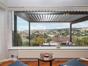 Een balkon met uitzicht op een stad, een tafel met een kopje en gebak, en een decoratie van een schip.