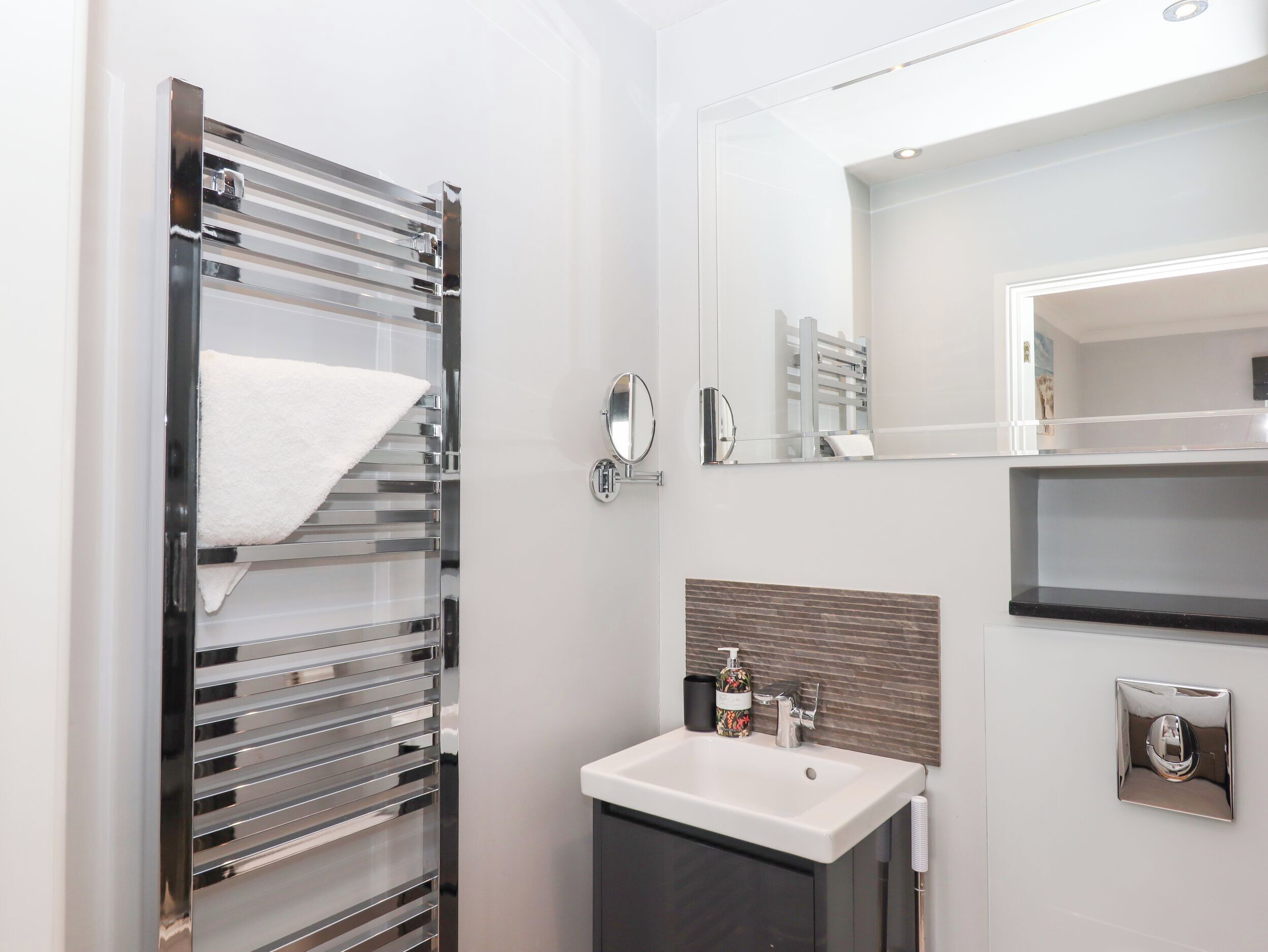 Een moderne badkamer met een chromen handdoekhouder, een witte wastafel, een spiegel, en een handdoek aan de houder.