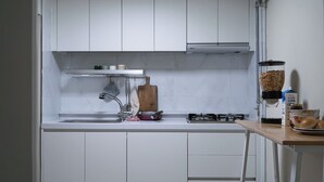 Una cocina con armarios blancos, un lavamanos de acero inoxidable, una tabla de cortar de madera, una estufa a gas y un bol de harina sobre la encimera.