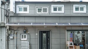 Un edificio de fachada gris, con varias ventanas y una puerta de acceso visible.