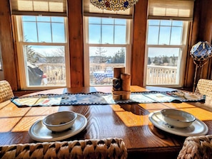 A dining table with two bowls, a woven placemat, and a view of a deck through large windows.