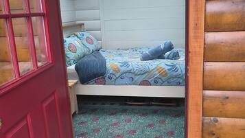 Quarto aconchegante com cama, porta vermelha e parede de madeira.