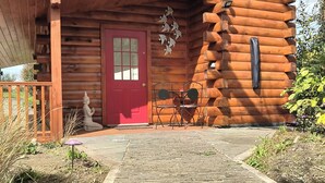 Una cabaña rústica de madera con puerta roja, un pequeño porche y un sendero de piedra que conduce a la entrada.
