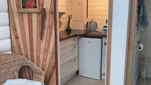 Una habitación acogedora con una pared de madera decorativa, un sillón de mimbre, una kitchenette pequeña y una cama con colcha colorida.