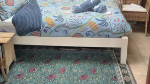Un dormitorio con cama, una silla y un tapete estampado.