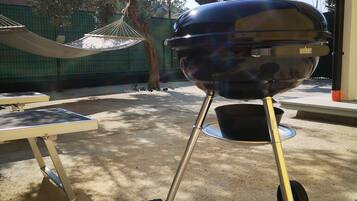 Una barbacoa Weber a l'exterior, amb una cadira espanyola i una taula a prop.