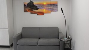 A modern living room with a grey sofa, a wall-mounted artwork depicting a sunset over the ocean, and a floor lamp. - AGAS Exclusive Apartment (Catanzaro)