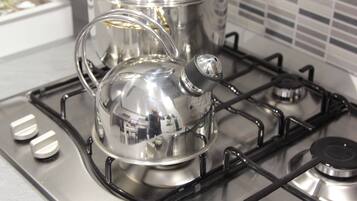 A stainless steel kettle on a gas stove with three burners.