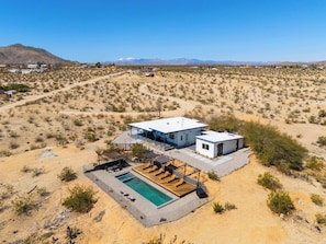 A desert landscape with a modern house featuring a pool, outdoor seating, and a covered patio. - Casa Azul | Joshua Tree | Swim | Relax | Recharge (Joshua Tree)