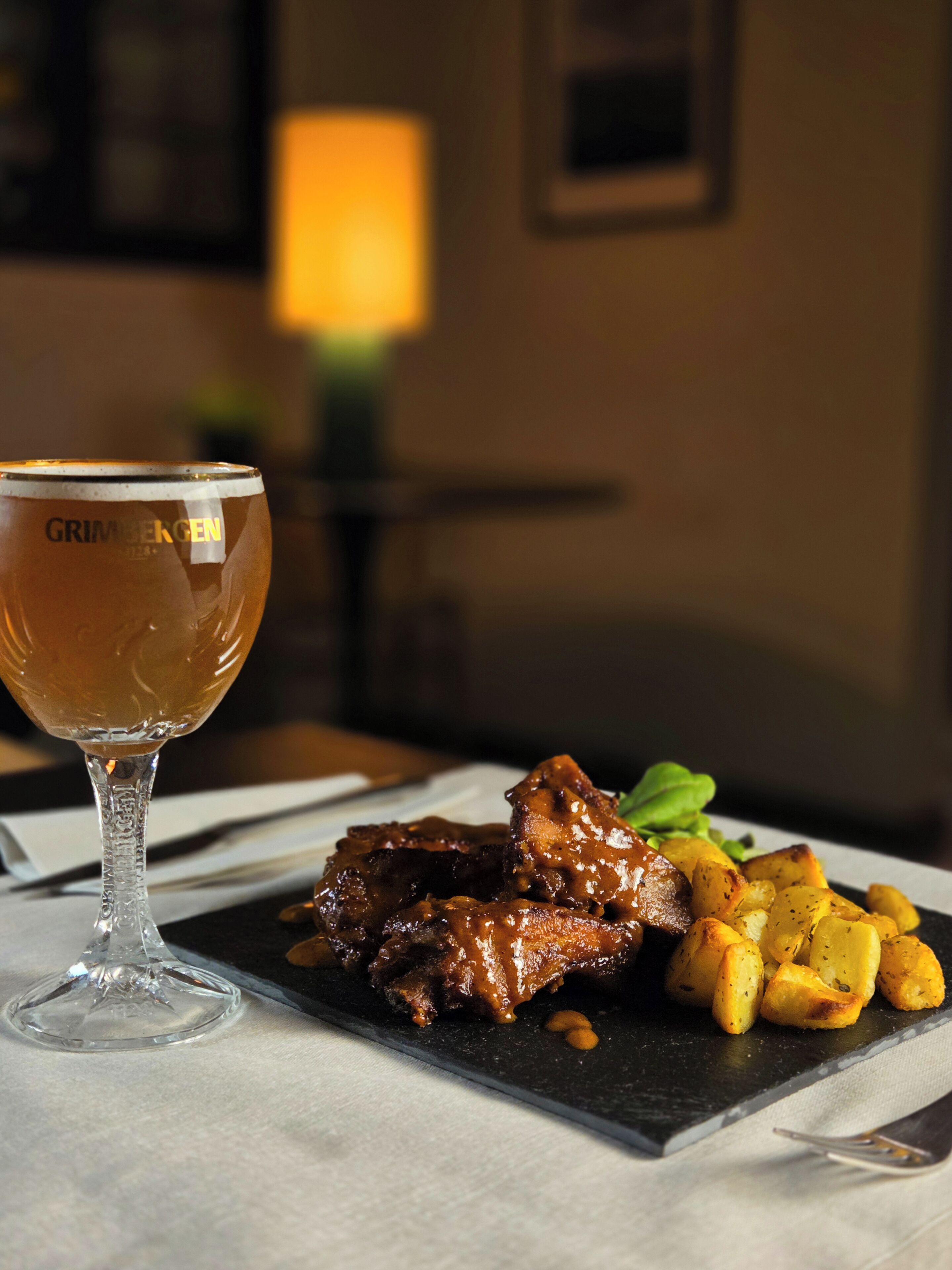 A glass of beer with a label, a plate of roasted meat, and potatoes.