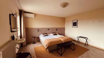 A hotel room with a bed, bedside table, chair, radiator, and a picture on the wall.