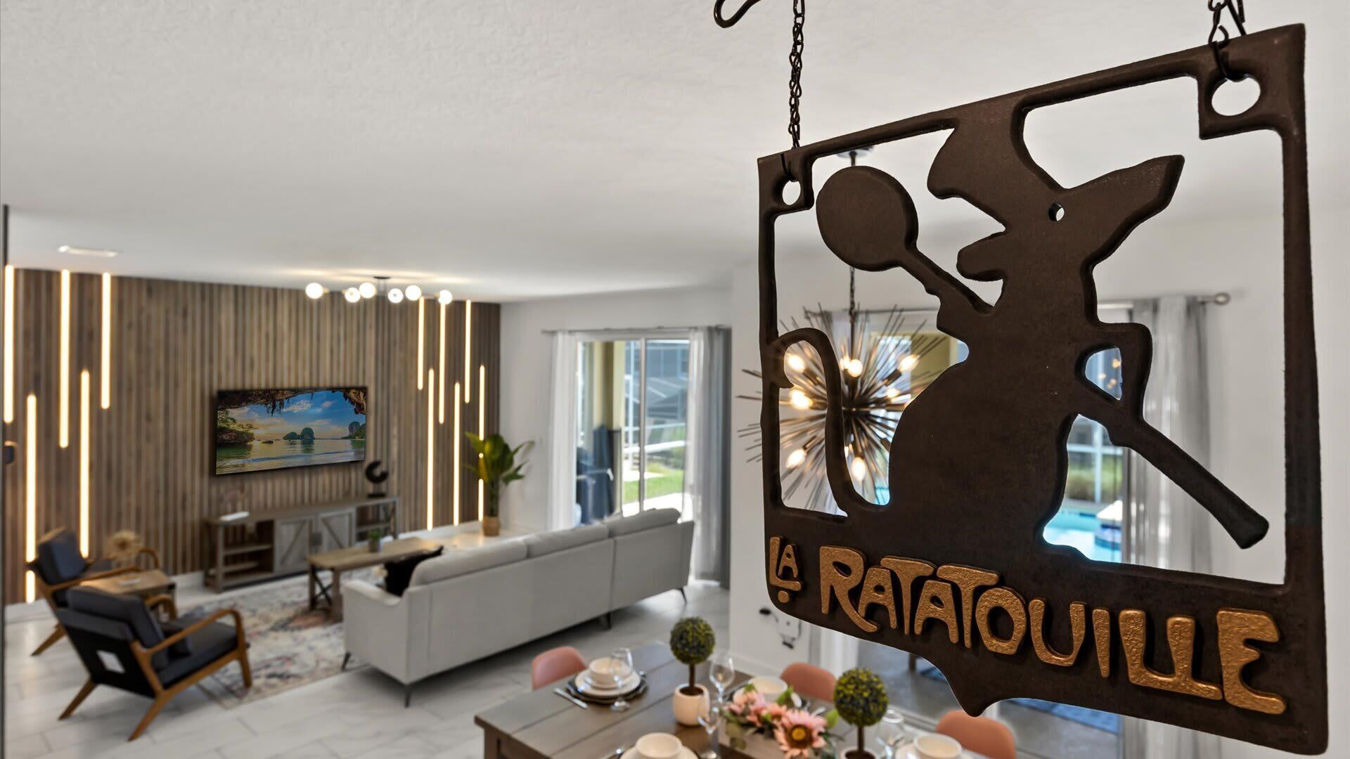 A modern living room with a sofa, chairs, a dining table set, and a hanging sign reading 'La Ratatouille'.
