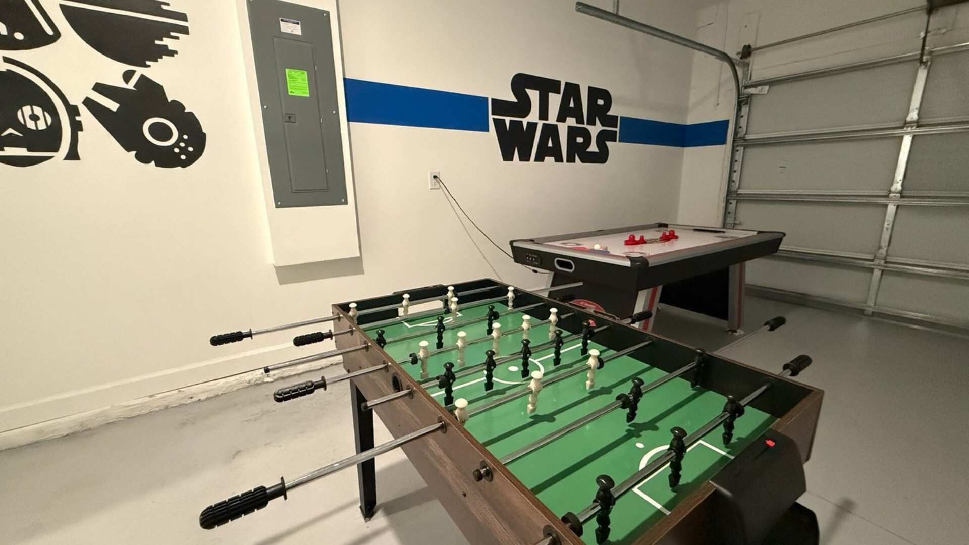 A room with a foosball table, Star Wars wall art, and a utility panel.