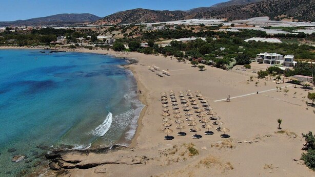 Una spiaggia con acque cristalline blu, una riva sabbiosa e una fila di ombrelloni.