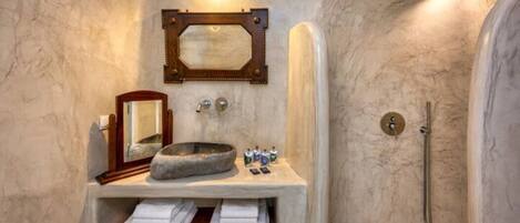 A bathroom with a stone sink, a mirror, and a shower.