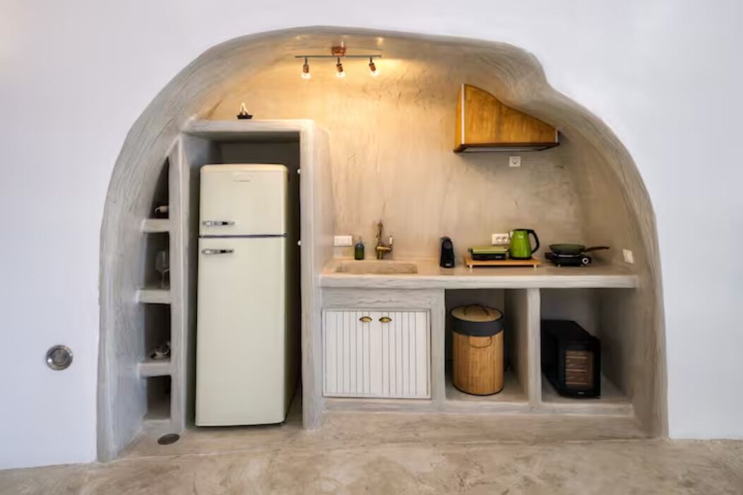 A compact kitchen with a white refrigerator, wooden cabinets, and a small countertop with a kettle and a coffee maker.