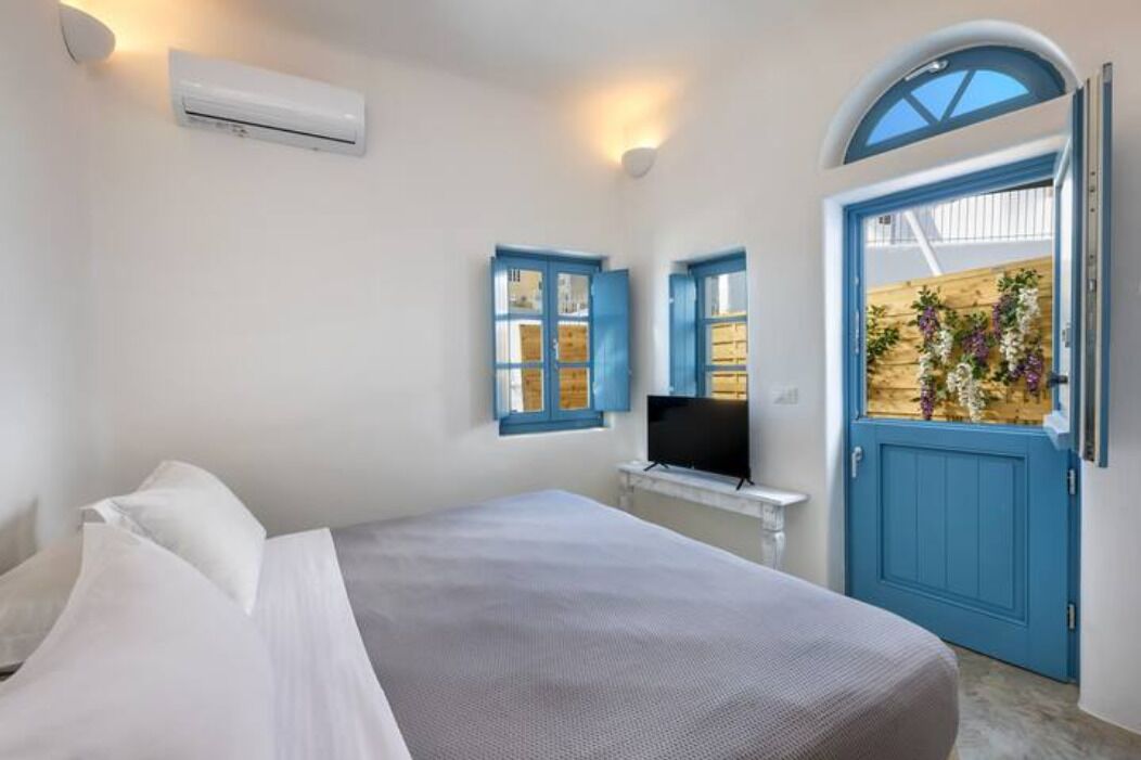 A bedroom with a bed, a TV, a blue door, and a wall-mounted air conditioner.