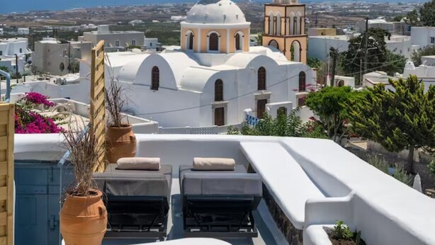A rooftop terrace with lounge chairs, a view of a white-domed building, and a clear blue sky.