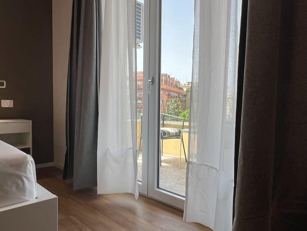 A room with a bed, a small table, and a sliding glass door leading to an outdoor area with a chair and a table.