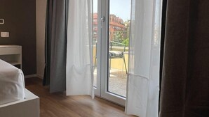 A room with a bed, a small table, and a sliding glass door leading to an outdoor area with a chair and a table.