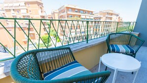 A balcony with two wicker chairs and a small round table, overlooking a residential area with multi-story buildings.