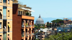 A multi-story building with balconies, a dome structure in the background, and a clear sky.