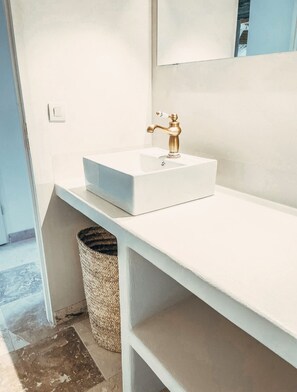 Une salle de bain moderne avec un lavabo blanc, un robinet doré et un miroir au-dessus.