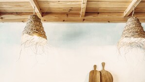 Une cuisine avec un plan de travail bleu clair, un évier blanc et des armoires en bois. On y trouve deux luminaires suspendus et deux planches à découper en bois posées sur le plan de travail.