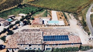 Vue aérienne d’une propriété dotée d’une piscine, de panneaux solaires et de bâtiments aux toits recouverts de tuiles en terre cuite.