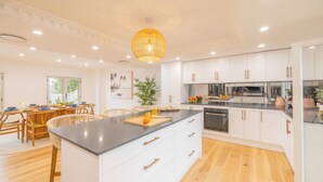 Une cuisine moderne avec des meubles blancs, un îlot central et un coin repas doté de meubles en bois.