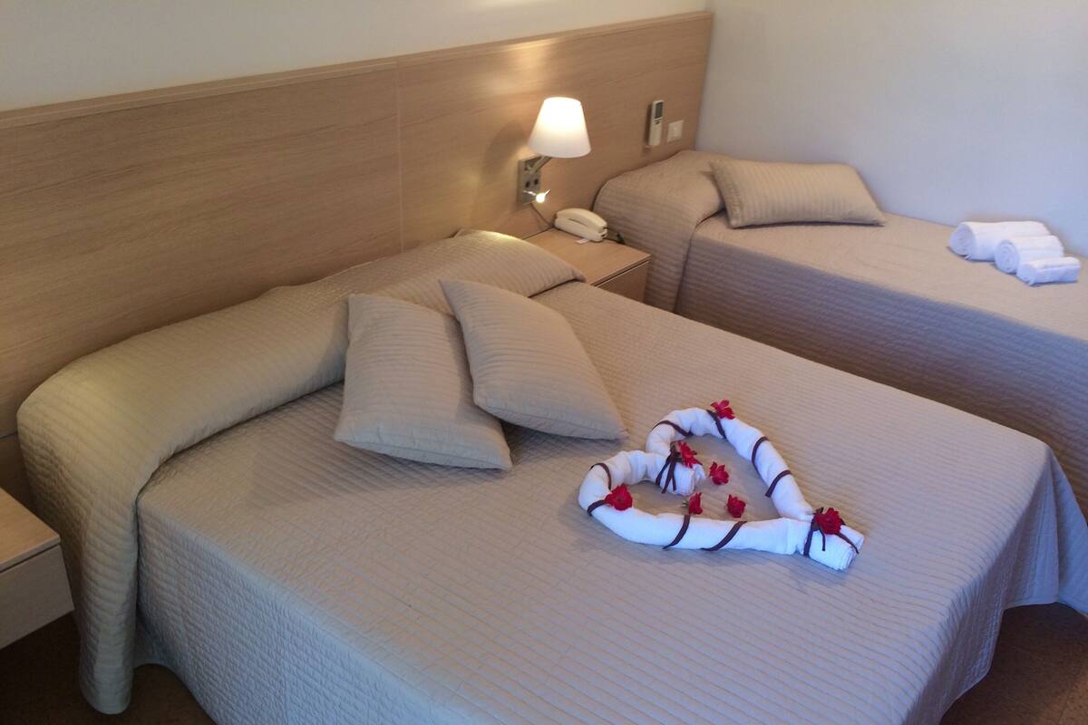 A hotel room with two beds, each with a pillow and a bedside table with a lamp.