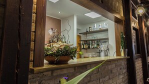 A bar area with a wooden counter, a potted plant, and shelves with bottles and glasses. - Hotel La Cantinella (Ostra)