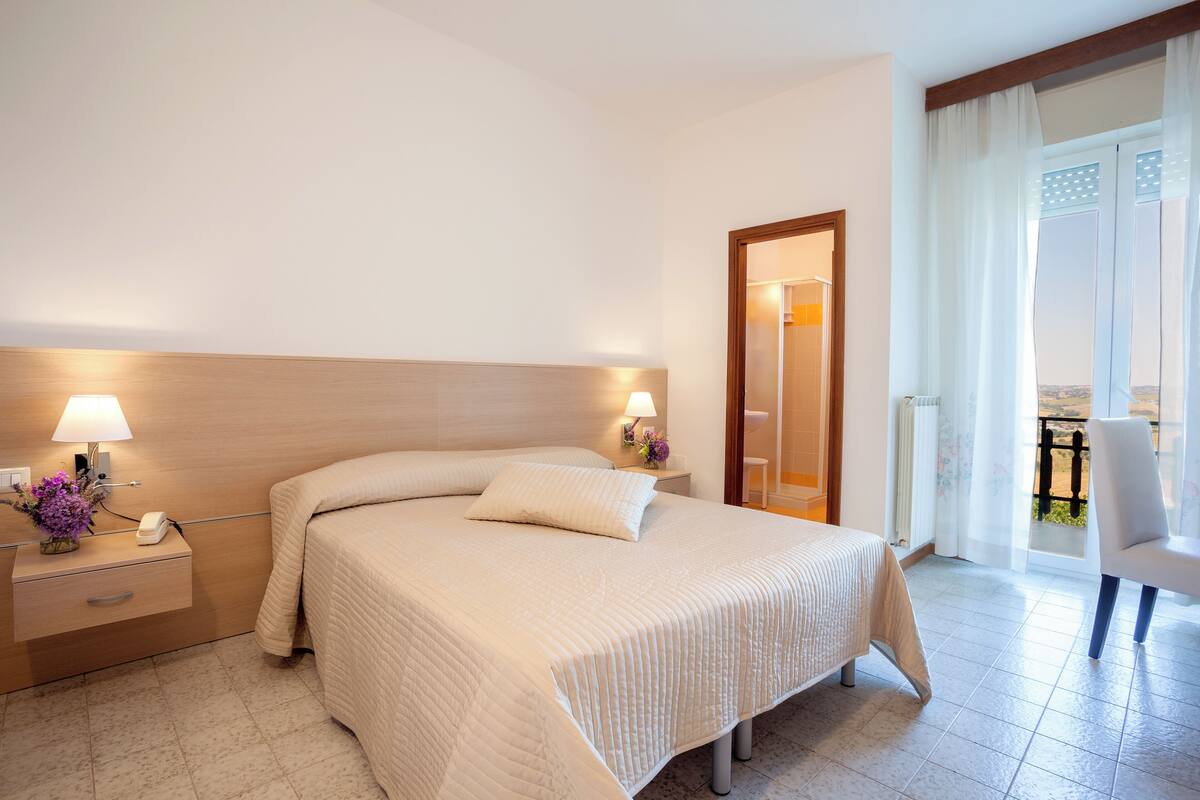 A hotel room with a large bed, bedside lamps, a nightstand, and a view of the balcony.