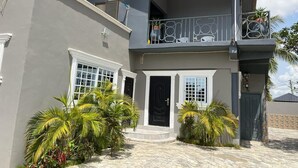 A two-story house with a balcony, satellite dish, and a well-maintained garden. - GHL. G Floor En-suites 2BR Sleep 4. WiFi, DSTV, SOLAR ,AC And Free Breakfast (Kasoa Ghana)