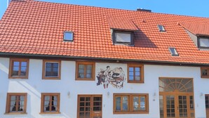 A building with a red-tiled roof, multiple windows, and a mural depicting a scene with people and animals.