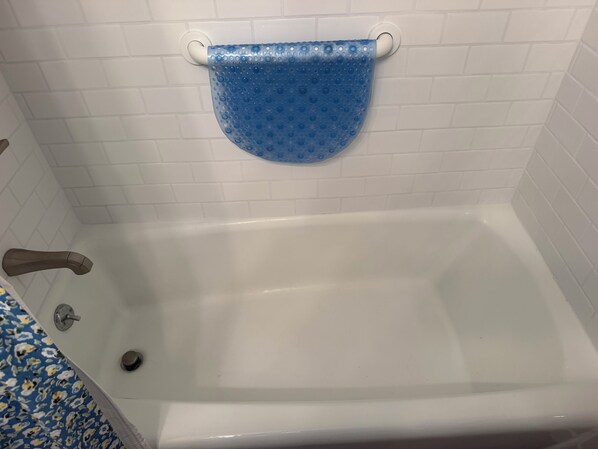 Una bañera con una alfombra de baño azul, un grifo y un desagüe.