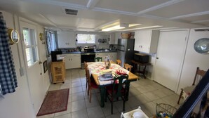 A compact kitchen with white cabinets, a dining table with chairs, a small refrigerator, and a microwave. - Idyllic 3-Bedroom Lake Front Cottage on Ford Lake (Fountain)