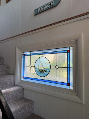 A staircase with a stained glass window depicting a sailboat on water. - Idyllic 3-Bedroom Lake Front Cottage on Ford Lake (Fountain)