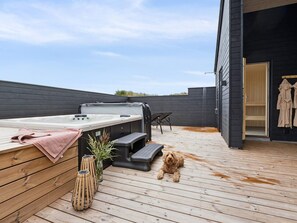 Eine Holzterrasse mit Whirlpool, Sitzgelegenheiten und einem Hund.