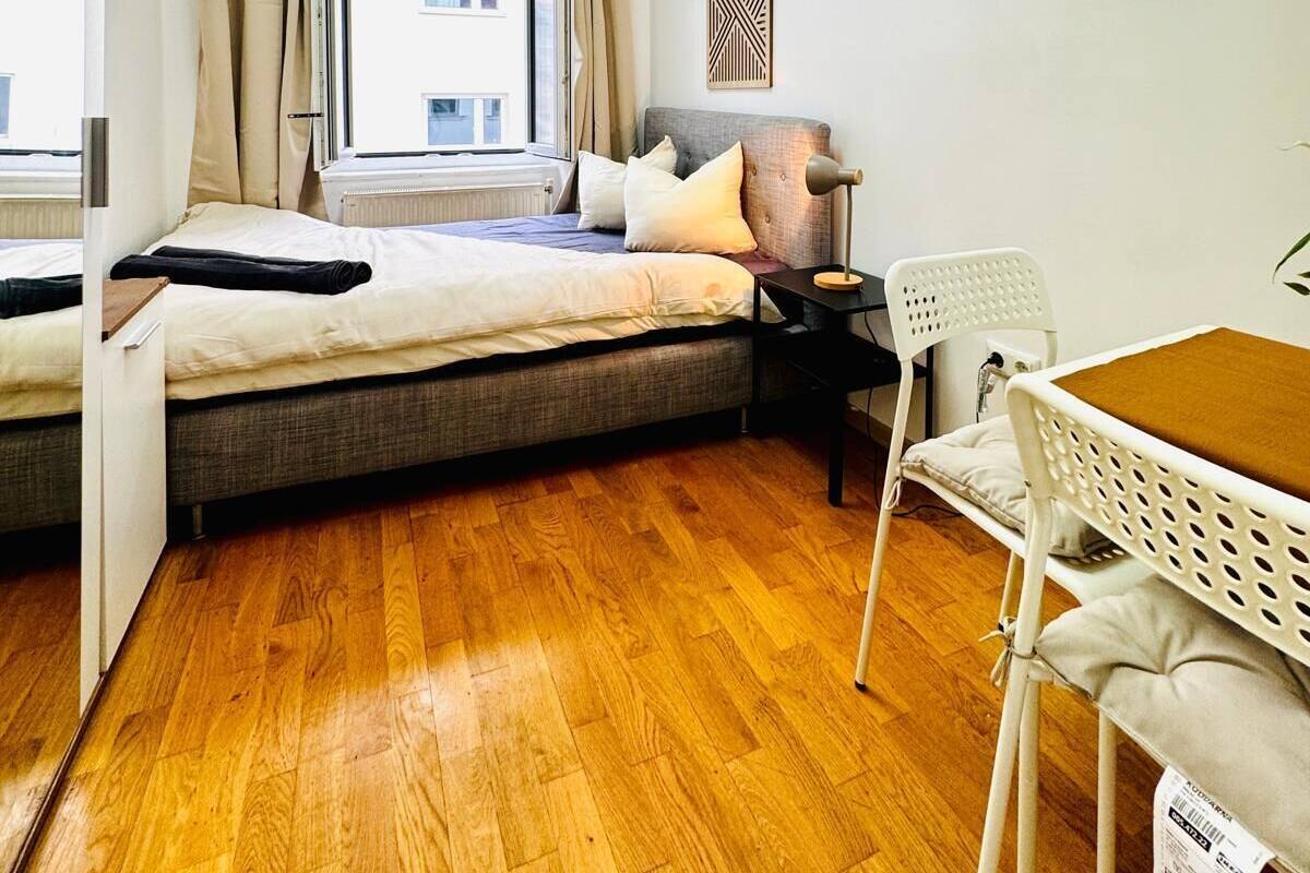 Un dormitorio compacto con cama, mesita de noche, silla y ventana con cortinas.