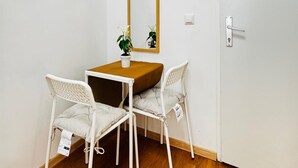 Een kleine kamer met een houten tafel, twee witte stoelen, een potplant, een spiegel en een witte deur.