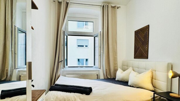 Een moderne hotelkamer met een groot bed, een nachtkastje met lamp, een raam met gordijnen en uitzicht op een gebouw.