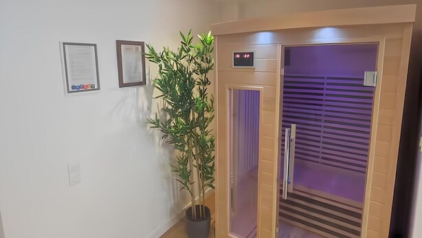 Un couloir avec une plante en pot, une horloge numérique et une porte coulissante violette qui donne sur une pièce.